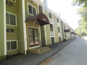 A slanted photograph of a large, green rental property with brown awnings.