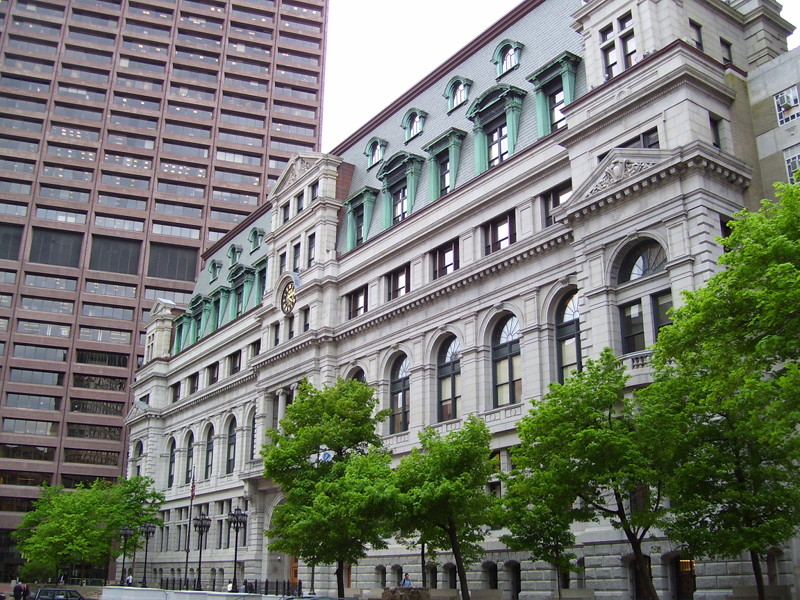 The John Adams Courthouse in Boston, Massachusetts is gray stone with a gold clock set above the entrance. Licensed CC BY 3 Swampyank at English Wikipedia.
